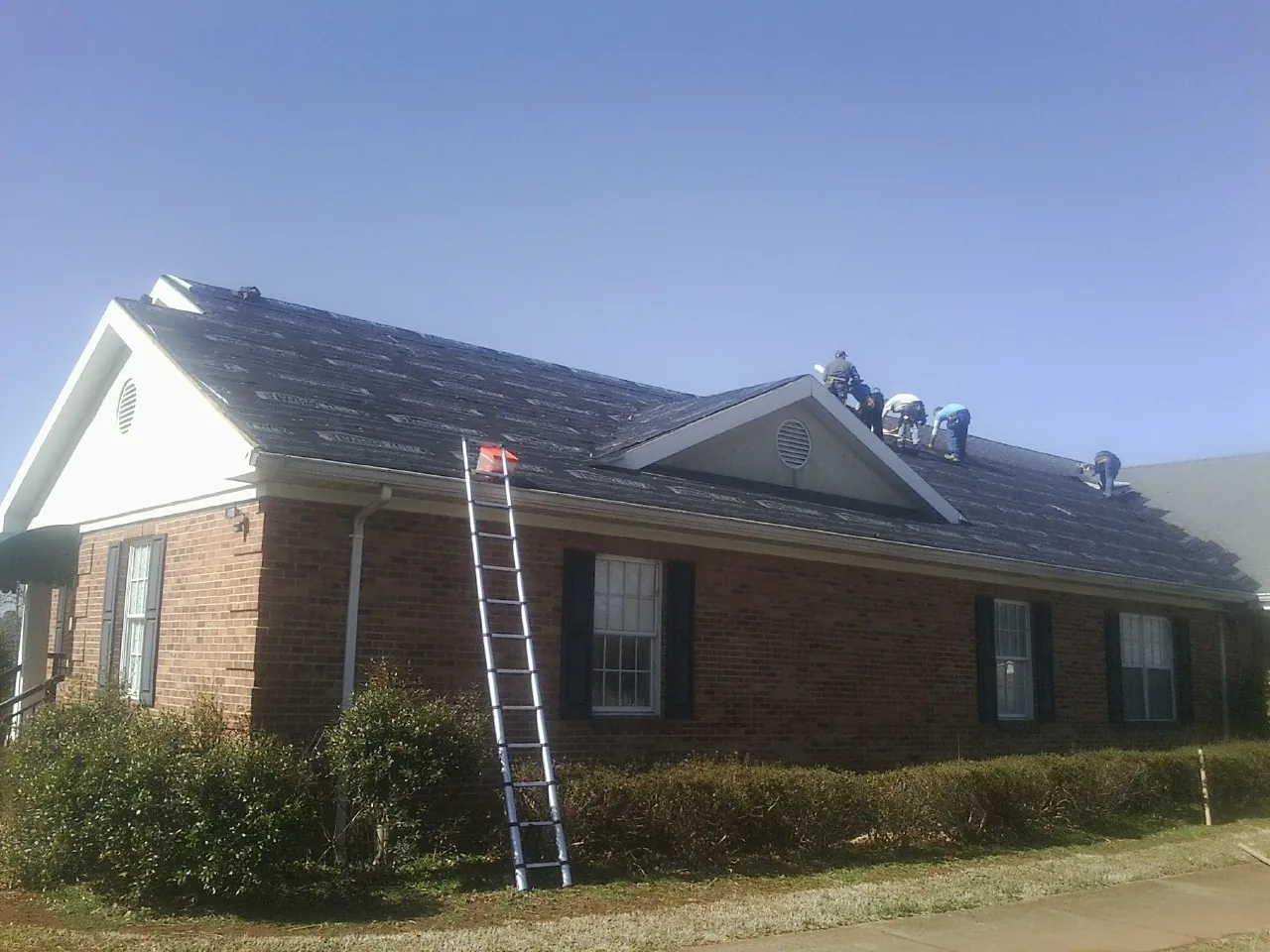 Crew tearing shingles off a brick ranch roof with a ladder set — Emergency Roof Repair work by our crew in Lisbon