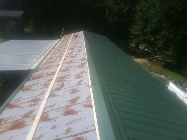 Old rusted panels beside newly installed green metal roofing — Wind Damage Roof Repair by Roofing Brothers in Lisbon